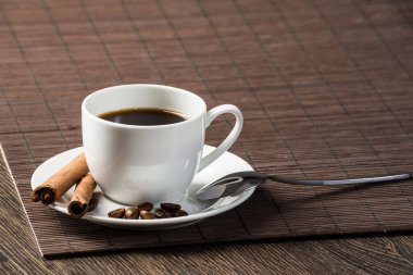 Tahta masada bambu hasırlı baharatlı sert doğal kahve. Kahve çekirdekleri ve tarçın çubukları beyaz porselen tabakta. Lokantada doğal aromatik sıcak içeceği kapat. Sabah kahve molası.