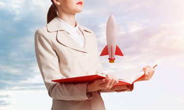 Açık kitapta roket gemisini gösteren kadın. Sembol başlangıç şirketi olarak roket fırlatma. Yeni yaratıcı proje konsepti. Skyscape arka planda beyaz iş elbisesi giymiş kadın. İş inovasyonu.