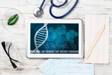 Modern tıp laboratuarında insan genetik araştırması. Ekranda DNA sarmal yapısı olan tablet bilgisayar. Ahşap masada steteskop ve kardiyogram. Tıbbi teşhisler ve hasta genom testi.