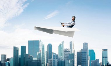 Korkmuş pilot, ağzı açık, kağıt düzlemde oturuyor ve direksiyonu tutuyor. Havacı mavi gökyüzünde iş merkezi üzerinde kağıt uçak sürüş. Yüksek gökdelenler ve ofis binaları ile Cityscape.