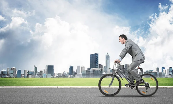Businessman hurry to work by bike. Man wearing business suit riding bicycle on countryside asphalt road. Cyclist on background of cityscape and blue sky. Eco-friendly transport and outdoor activity