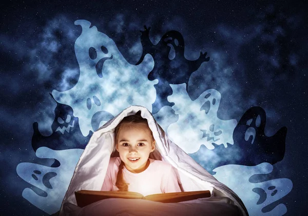 快乐的小女孩睡觉前在床上看书 手电筒藏在毯子下的孩子 穿着睡衣的微笑女孩和有趣的鬼魂回到夜空 儿童阅读魔法童话 — 图库照片