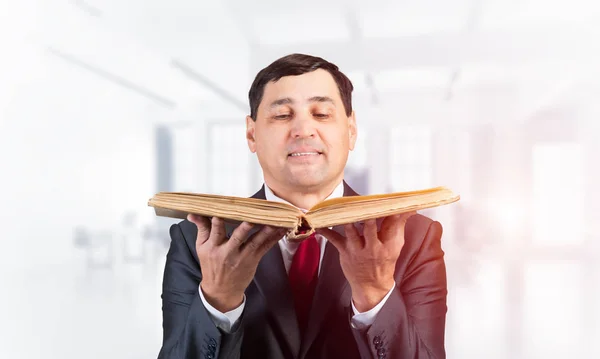 Senior businessman looking in open book. Portrait of adult man in business suit and tie standing in blurred office interior. Lawyer holding big legal regulation book. Professional business accounting.