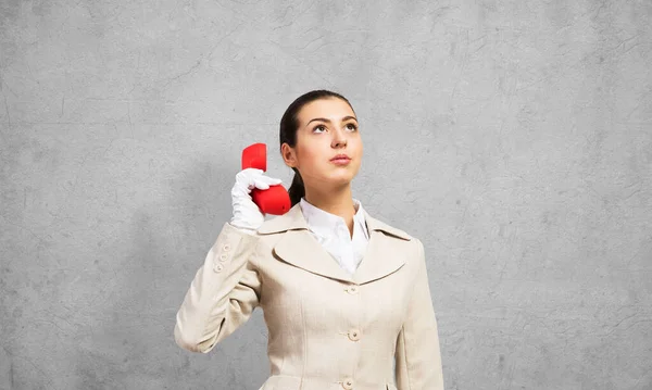 在灰色墙壁的背景下 迷人的女人拿着老式的红色手机 优雅的经营者身穿白色西装 手持固定电话 热线电话营销和商业通信 — 图库照片