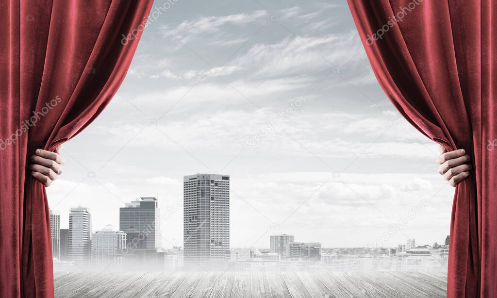 Human hand opens red velvet curtain to modern cityscape and cloudy sky