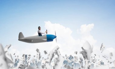 Memnun duygusal pilot küçük bir uçak kabinde oturan. Havacı şapkalı mutlu adam ve gözlükler, grafiklerle düşen kağıt kağıtların üzerinde pervane düzlemi sürüyor. Yüksek binalarile modern metropol