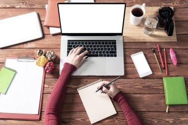 Ofis masasındaki not defterine yazan iş kadını. Çevrimiçi iş öğrenimi ve eğitim. Kadın eli, dizüstü bilgisayarı ve belgeleri olan düz ofis işyeri. Dijital teknoloji ve ortak çalışma alanı
