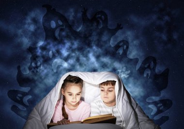 Dalmış küçük çocuklar yatakta kitap okuyorlar. Erkek ve kız kardeş battaniyenin altında saklanıyorlar. Pijama ve derin mavi arka plan üzerinde hayali canavarlar korkulan çocuklar. Çocuk masalları okuma.