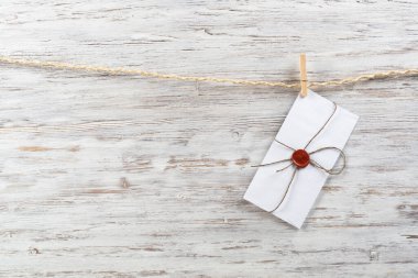 Çamaşır mandallarıyla ipte sallanan beyaz klasik zarf. Ahşap arka planda eski bir aşk ilanı. Balmumu mühürlü eski mektup zarfı. Romantik düğün davetiyesi.