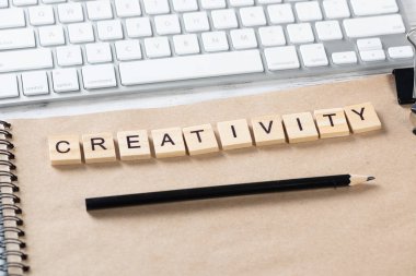 Küpler üzerindeki harflerle yaratıcılık ve yenilik kavramı. Ofisin çalışma alanı hala dolu. Bilgisayar klavyesi ve spiral not defteri olan düz, eski, tahta bir masa. Beyin fırtınası ve fikirler üretimi.