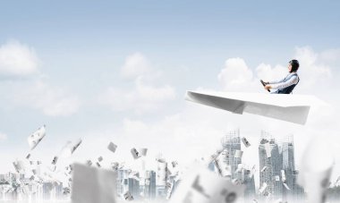 Havacı mavi gökyüzünde iş merkezi üzerinde kağıt uçak sürüş. İş belgeleriyle çalışmak. Gökdelenlerin arka planına düşen kağıtlar. Deri kasklı pilot kağıt düzlemde oturuyor