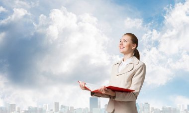 Şehir manzarası ve mavi gökyüzü arka planda açık defter tutan çekici kadın. Elinde açık kitap ile beyaz iş elbisesi zarif genç kadın. Şirkette staj ve uygulama.