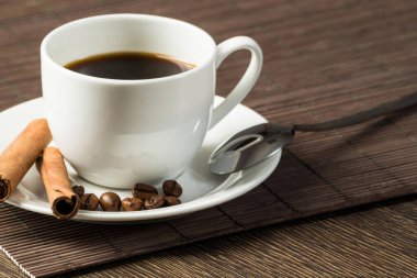 Bambu mat ile ahşap masada espresso kahve fincan. Kahve çekirdekleri ve tarçın beyaz porselen tabak üzerinde sopa. Restoranda doğal aromatik sıcak içecek kapatın. Sabah kahve molası.