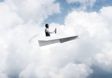 Pilot deri kask ve gözlük mavi bulutlu gökyüzünün arka planda kağıt uçak sürüş. Dünyayı dolaşıyor. Küçük kağıttan uçakta uçan komik adam. Kabarık bulutlu gökyüzü panoraması.