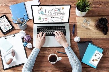 Ofis çalışma alanı ile multimedya eğitim kavramı. Düz tahta masa, dizüstü bilgisayar, kadın eli ve bir fincan kahve. Bilgisayarda çalışan bir iş kadını. Çevrimiçi webinar ya da konferans web yayını