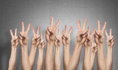 Zafer jestini gösteren bir sıra insan eli. Galibiyet ya da zafer işareti grubu. İnsan elleri gri duvarın arka planında siler. Birçok kol birlikte kaldırdı ve mevcut popüler jest.