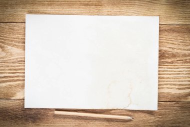 Tahta masanın üzerinde duran bir yaprak kağıt. Boş beyaz a4 formatlı kalem kağıdı. Dokulu doğal ahşap arka plan. Tasarım için klasik kopyalama alanı. İş planlaması ve fikir üretimi.