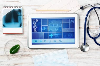 Modern sosyal sağlık sigortası programı. Ekranda sağlık uygulaması arayüzü olan tablet bilgisayar. Stetoskop, röntgen görüntüsü ve kardiyogram tahta masada. Dijital sağlık teknolojileri.