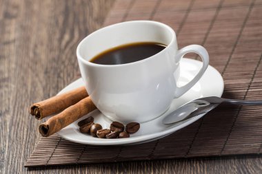 Tahta masada bambu hasırlı baharatlı sert doğal kahve. Kahve çekirdekleri ve tarçın çubukları beyaz porselen tabakta. Lokantada doğal aromatik sıcak içeceği kapat. Sabah kahve molası.
