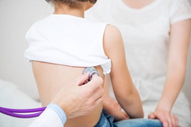 Doktor çocuğu muayene ediyor ve hastanede steteskopla ciğerlerini dinliyor. Küçük kızın tıbbi muayenesi. Profesyonel klinik tanılama ve tedavi. Aile Sağlık Merkezi
