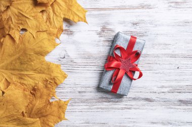 Hediye kutusu ve sarı sonbahar yapraklarıyla düz bir kompozisyon sergiliyordu. Eski ahşap masanın üstünde süslü kırmızı kurdele var. Şükran günün kutlu olsun. Güz mevsiminin durgun yaşamı.