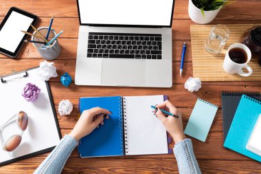 Ofis masasındaki not defterine yazan iş kadını. Çevrimiçi iş öğrenimi ve eğitim. Kadın eli, dizüstü bilgisayarı ve belgeleri olan düz ofis işyeri. Dijital teknoloji ve ortak çalışma alanı
