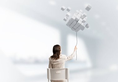 Üç boyutlu küplerden alınan ipin soyut bileşiminden tutulan kadın. Beyaz takım elbiseli uzun saçlı kadın, açık ofiste beyaz sandalyede oturuyor. Dijital teknoloji ve yenilik çözümleri.