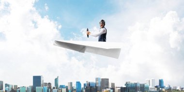 Kağıt uçakta oturan pilot ile iş motivasyonu kavramı. Havacı şapkalı komik adam ve şehrin üzerinde kağıt uçak süren gözlükler. Rüyada gökyüzünde uçmak. Yüksek binalarile modern megapolis.