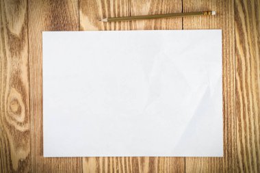Tahta masanın üzerinde duran bir yaprak kağıt. Boş beyaz a4 formatlı kalem kağıdı. Dokulu doğal ahşap arka plan. Tasarım için klasik kopyalama alanı. İş planlaması ve fikir üretimi.