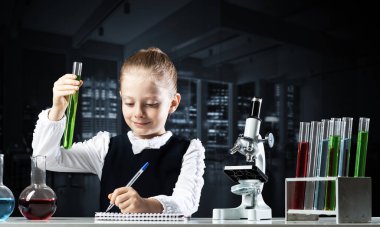 Not defterinde test tüpü yazan küçük bir bilim adamı kız. Okulda araştırma ve eğitim. Mikroskop ve cam mataralı kimya laboratuvarı. Öğrenci kız kimya dersinde deney yapıyor..