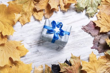 Hediye kutusu ve sarı sonbahar yapraklı düz sonbahar kompozisyonu. Klasik ahşap masada süslü mavi kurdele kurdelesi. Şükran günün kutlu olsun. Sonbahar indirimi reklamı.