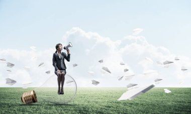 Megafonlu, ampulün üzerinde oturan genç bir kadın. Kadın hoparlör uçan kağıt uçaklar ile yeşil çayır üzerinde yeni hizmet veya ürün reklam. İş adamı hoparlörden bağırıyor. İş duyurusu