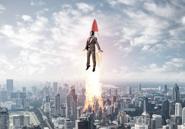 Havacı şapkalı bir iş adamı roketle uçuyor. İlerleme ve yenilik teknolojisi. Modern şehrin üzerinde mavi gökyüzünde jetpack roketiyle uçan bir şirket işadamı. Liderlik motivasyon kavramı.