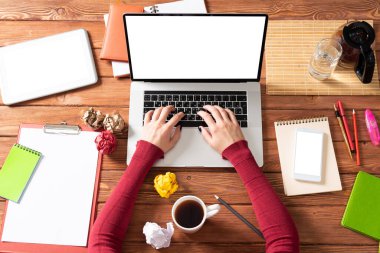 Kadın eli ile modern ofis çalışma alanı. Düz tahta masa, dizüstü bilgisayarlı klavye, bir fincan kahve ve buruşuk kağıt toplarla. İş kadını elleri boş ekranla bilgisayarda çalışıyor.