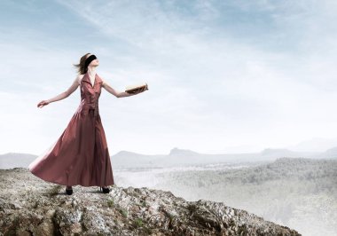 Kırmızı uzun elbiseli genç bir kadın ve elinde kitapla gözleri bağlı.