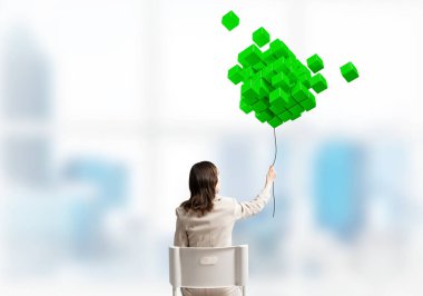 İple tutulan kadın 3 boyutlu küplerden soyut yeşil kompozisyon. Beyaz takım elbiseli uzun saçlı kadın, açık ofiste beyaz sandalyede oturuyor. Dijital teknoloji ve yenilik çözümleri.