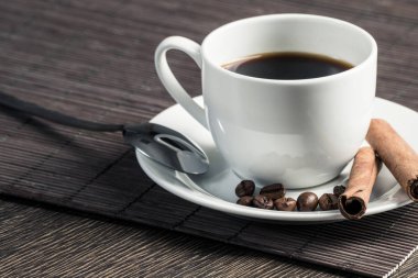 Bambu mat ile ahşap masada espresso kahve fincan. Kahve çekirdekleri ve tarçın beyaz porselen tabak üzerinde sopa. Restoranda doğal aromatik sıcak içecek kapatın. Sabah kahve molası.