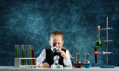 Kimya dersinde mikroskopla sınıfa bakan küçük bir bilim kadını. Cam mataralar ve test tüpleriyle okul kimya laboratuvarında. Öğrenci kız kimya dersinde deney yapıyor..