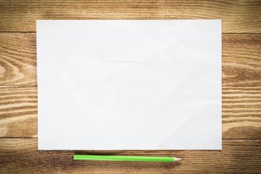 Tahta masanın üzerinde duran bir yaprak kağıt. Dikdörtgen, boş, eski, kurşun kalemli kağıt. Dokulu doğal ahşap arka plan. Tasarım için klasik kopyalama alanı. Sanatçı işyeri ve el çizimi becerileri