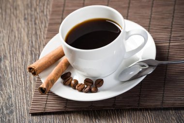 Bambu mat ile ahşap masada espresso kahve fincan. Kahve çekirdekleri ve tarçın beyaz porselen tabak üzerinde sopa. Restoranda doğal aromatik sıcak içecek kapatın. Sabah kahve molası.