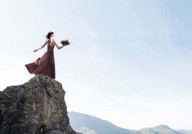 Kırmızı uzun elbiseli genç bir kadın ve elinde kitapla gözleri bağlı.