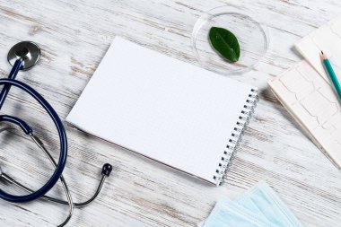 Doktor işyerindeki hasta muayenesi ve danışma konsepti. Spiral not defteri, tek kullanımlık yüz maskesi, steteskop ve tahta yüzeyde kardiyogram. Tıp merkezinde profesyonel sağlık hizmetleri.