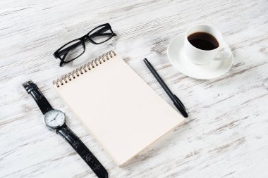 Bir fincan kahveyle ofis hayatının çalışma alanı kompozisyonu. Düz tahta masa, açık spiral defter, gözlük ve kalemle. Kafede kahve molası. Notlar için boş defter sayfası.