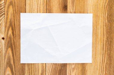 Ahşap masa üzerinde yatan kağıt levha ile Sanatçı işyeri. Boş kopyalama alanı ile dikdörtgen beyaz kağıt. Dokulu doğal ahşap arka plan üst görünümü. Reklam için sanat okulu şablonu