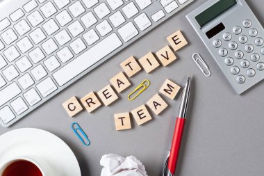 Küp üzerinde harflerle yaratıcı takım konsepti. Malzemelerle dolu ofis çalışma alanı. Düz gri yüzey, bilgisayar klavyesi ve hesap makinesiyle yatıyordu. İlham ve hayal gücü, iş dünyası takım çalışması