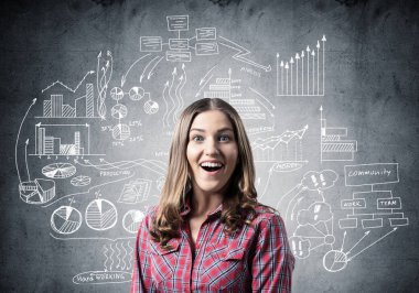 Gülümseyen güzel bir kız. Duygusal genç kadın yüz ifadesini şaşırttı. Finansal tablolar ve gri duvara iş karalamaları. Hoş bir kızın portresi kırmızı kareli gömlek giyer..