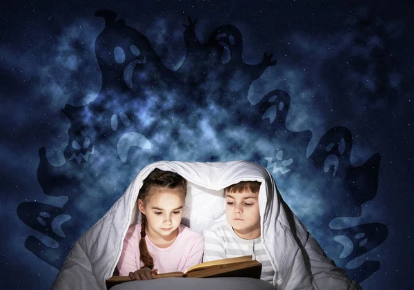 夢中の小さな子供たちがベッドで本を読んでいる 兄弟姉妹は毛布の下に隠れていた 深い青い背景にパジャマや架空のモンスターの恐ろしい子供たち おとぎ話を読む子供 — ストック写真