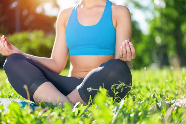女の子は緑の芝生の上で蓮のポーズで瞑想します ヨガの概念の練習 頭のないスポーツウェアを着た若い女体 夏の日にトレーニングと瞑想の屋外 健康的なライフスタイルとリラクゼーション — ストック写真