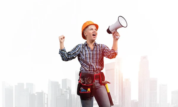 戴着安全帽的有表情的女人对着扩音器大喊 在雾蒙蒙的城市背景下张大嘴的年轻情感建筑工人的画像 新闻广播和广告 — 图库照片