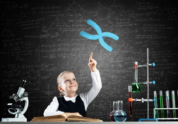 Little girl scientist with microscope on chalkboard background with x chromosome. Research and discovery concept. Elementary science class in modern school. Schoolgirl in schoolwear sitting at desk.